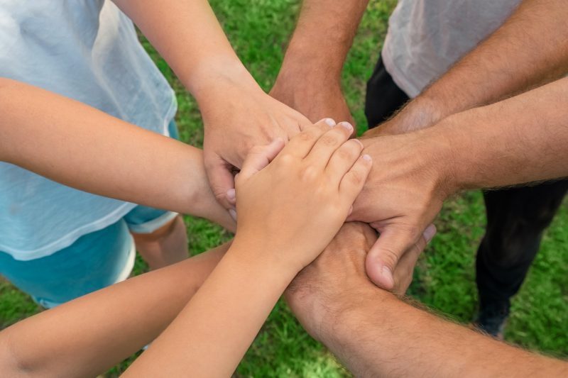 Joined hands as a team. Business teamwork. Close up group of multiracial friends meeting join hands together. Diversity people. Partnership volunteer community. Diverse multiethnic Partners. Top View. collaboration. Summer green grass background. Green lawn, meadow.