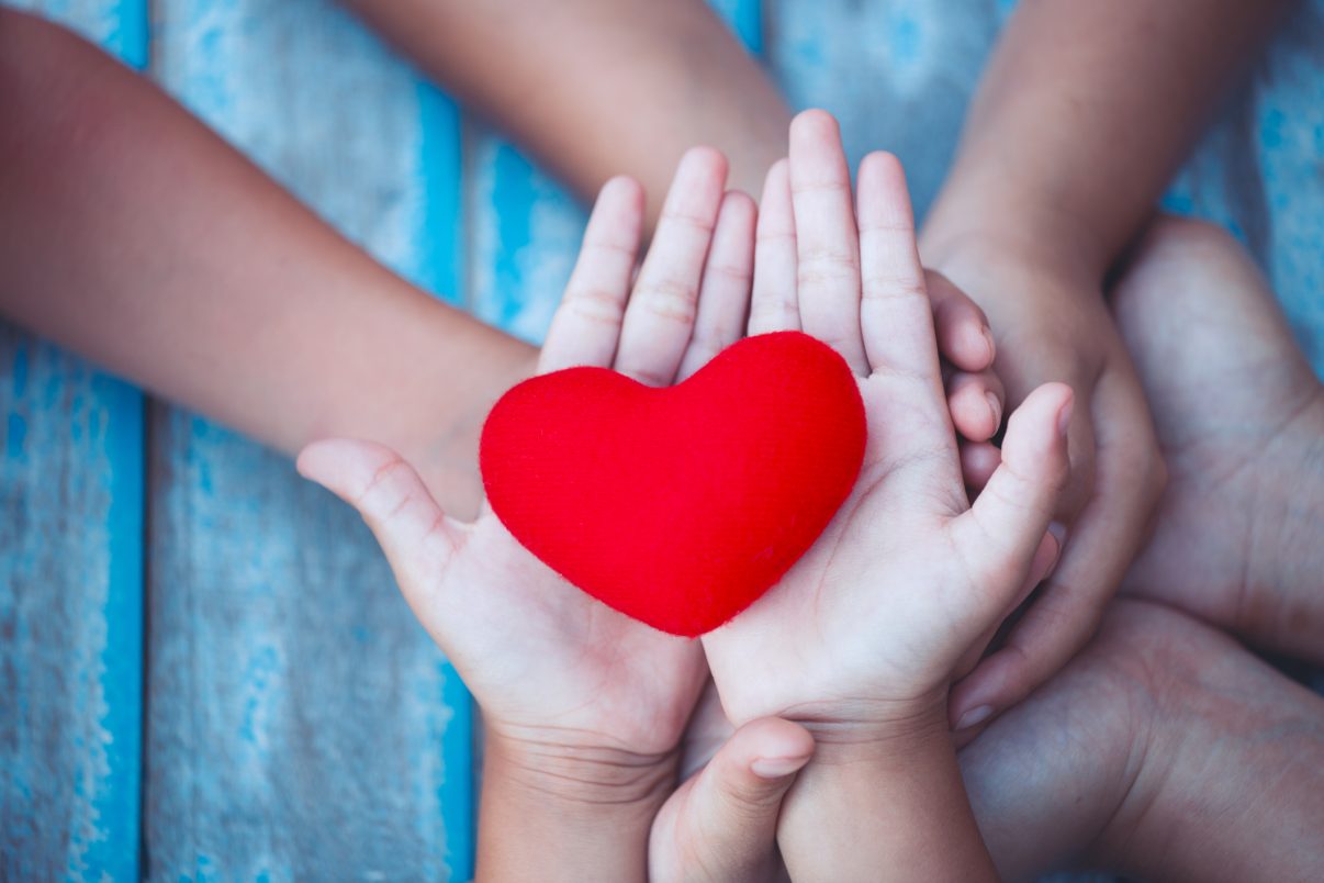 Red heart in child and parent hands with love and harmony. Family holding red heart together